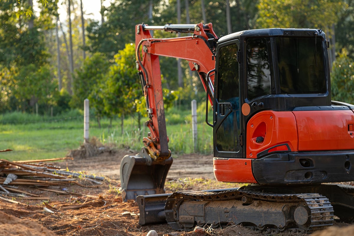 A vibrant orange and black mini excavator stands ready on a dirt construction site, with a pile of wooden debris nearby