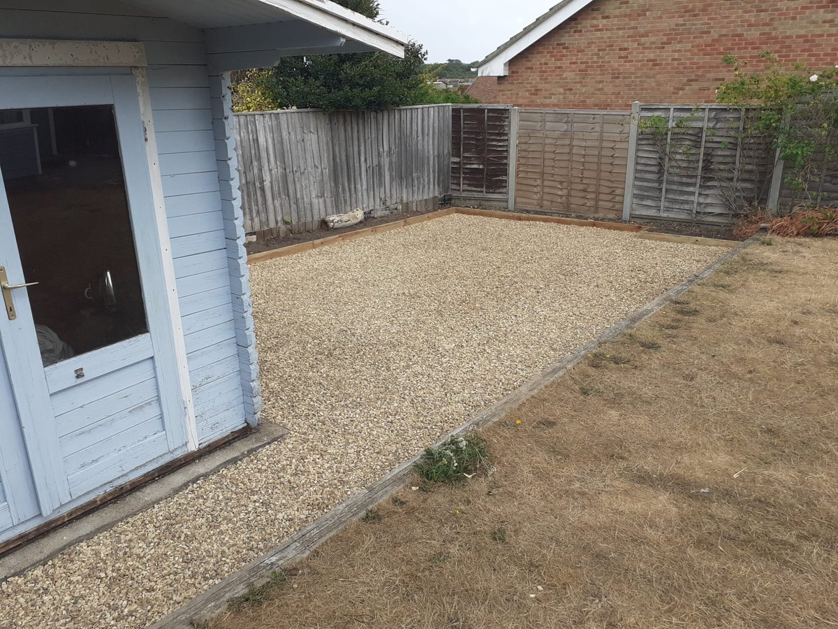 A residential backyard with gravel surface, white storage shed, wooden fences, and brick house wall