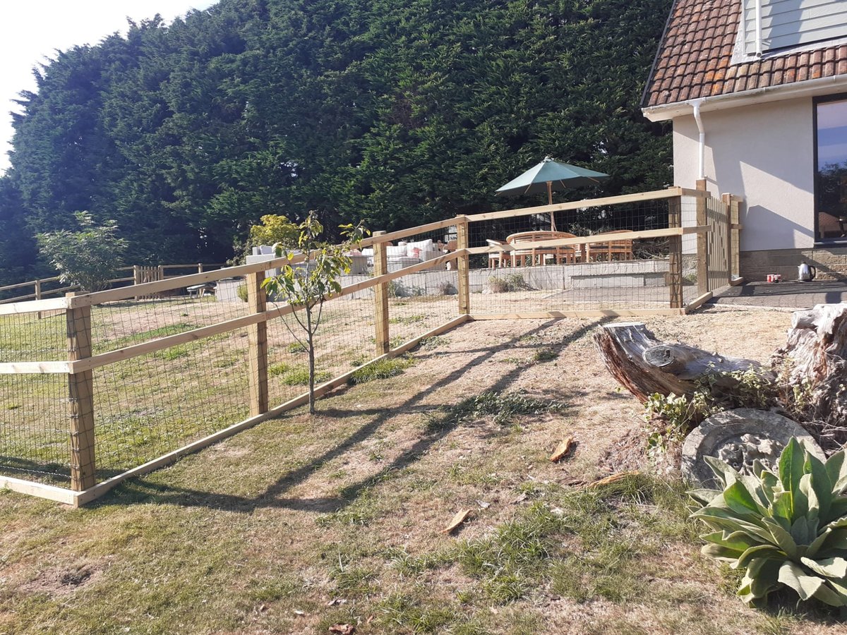 Wooden fenced equestrian property with covered riding arena, paddocks, and white residential building on landscaped grounds