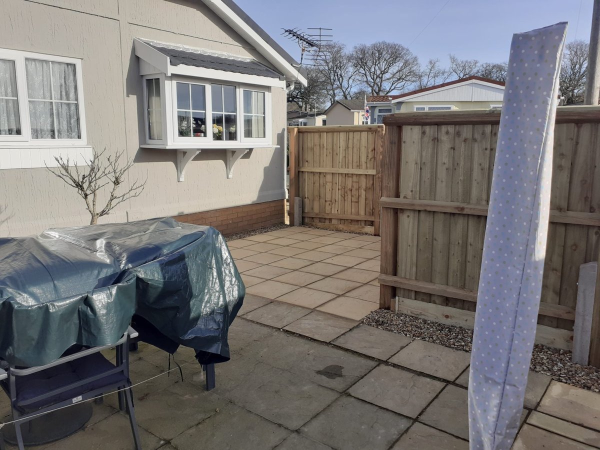 Residential patio with covered furniture, wooden fencing, and access to cream-coloured house with bay window