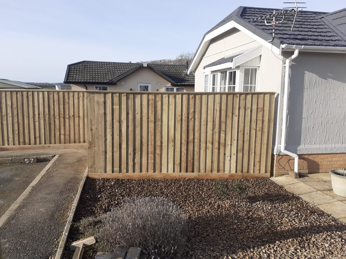 Tan wooden closeboard fence enclosing a gravel driveway with residential houses in the background