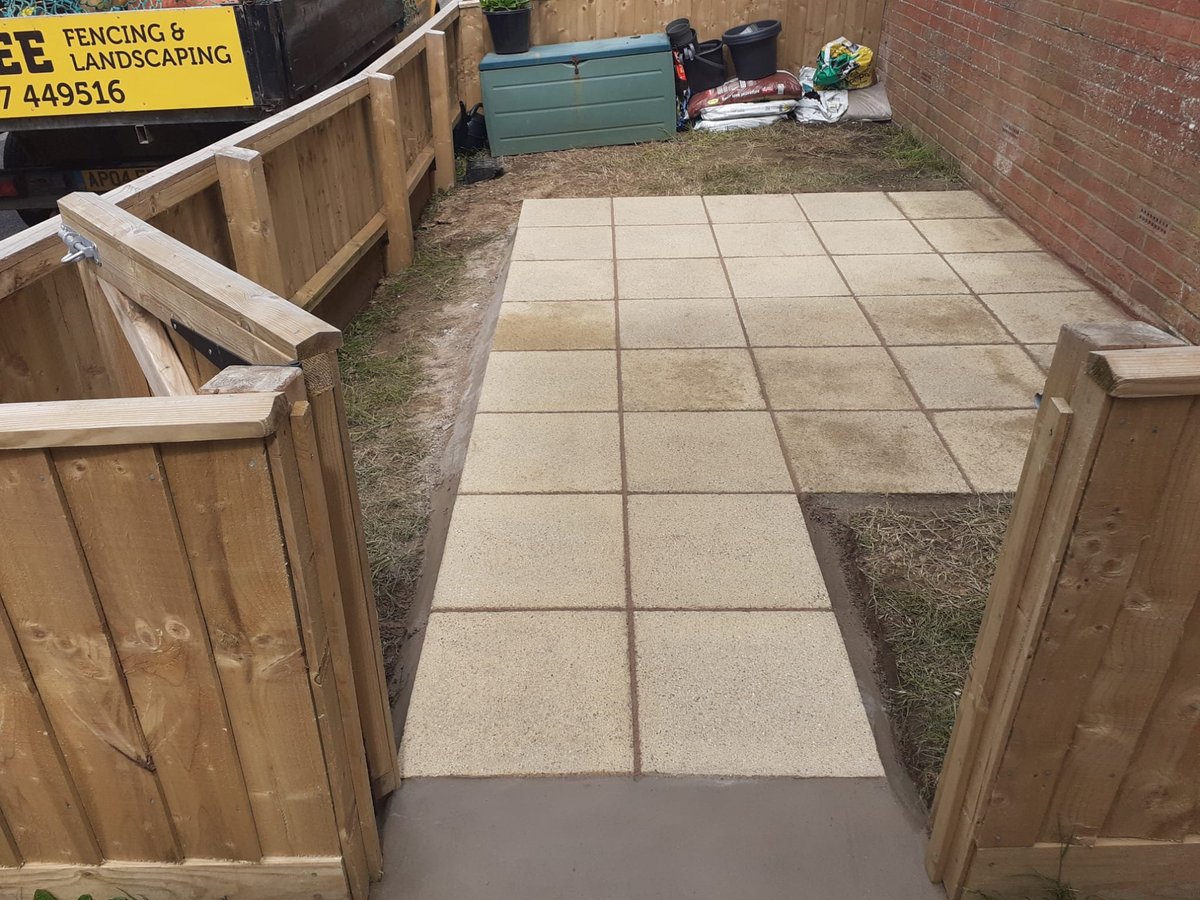 Newly laid patio with square pavers surrounded by wooden fence panels, with landscaping supplies visible in background