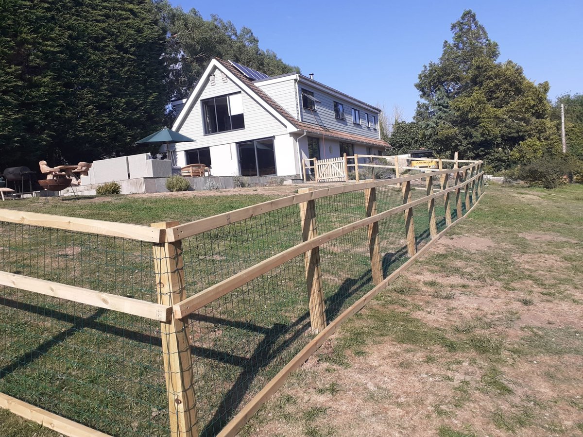 White farmhouse with wooden rail fencing in foreground, surrounded by green grass and trees on sunny day