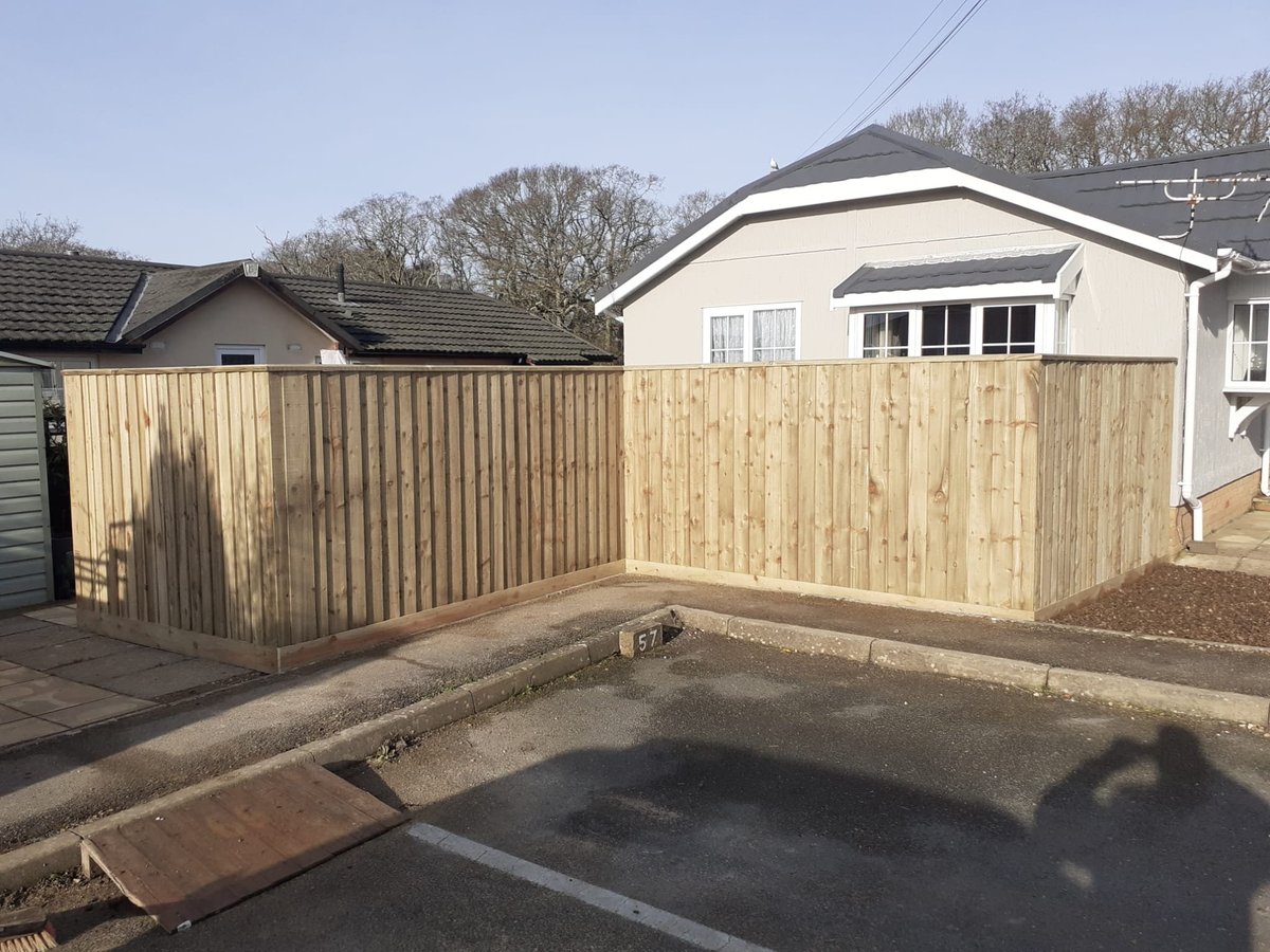 Residential backyard with new wooden fence, concrete patio foundation, and houses with bare trees in background